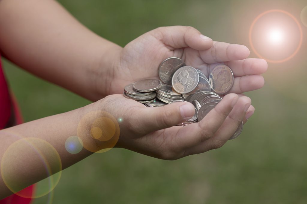 Mãos infantis segurando moedas, para representar a mentalidade de riqueza